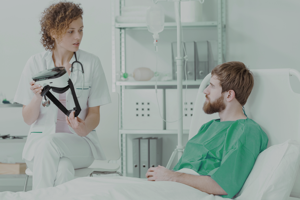 Healthcare professional showing a VR headset to a patient in a hospital bed for Remotion virtual rehabilitation therapy.