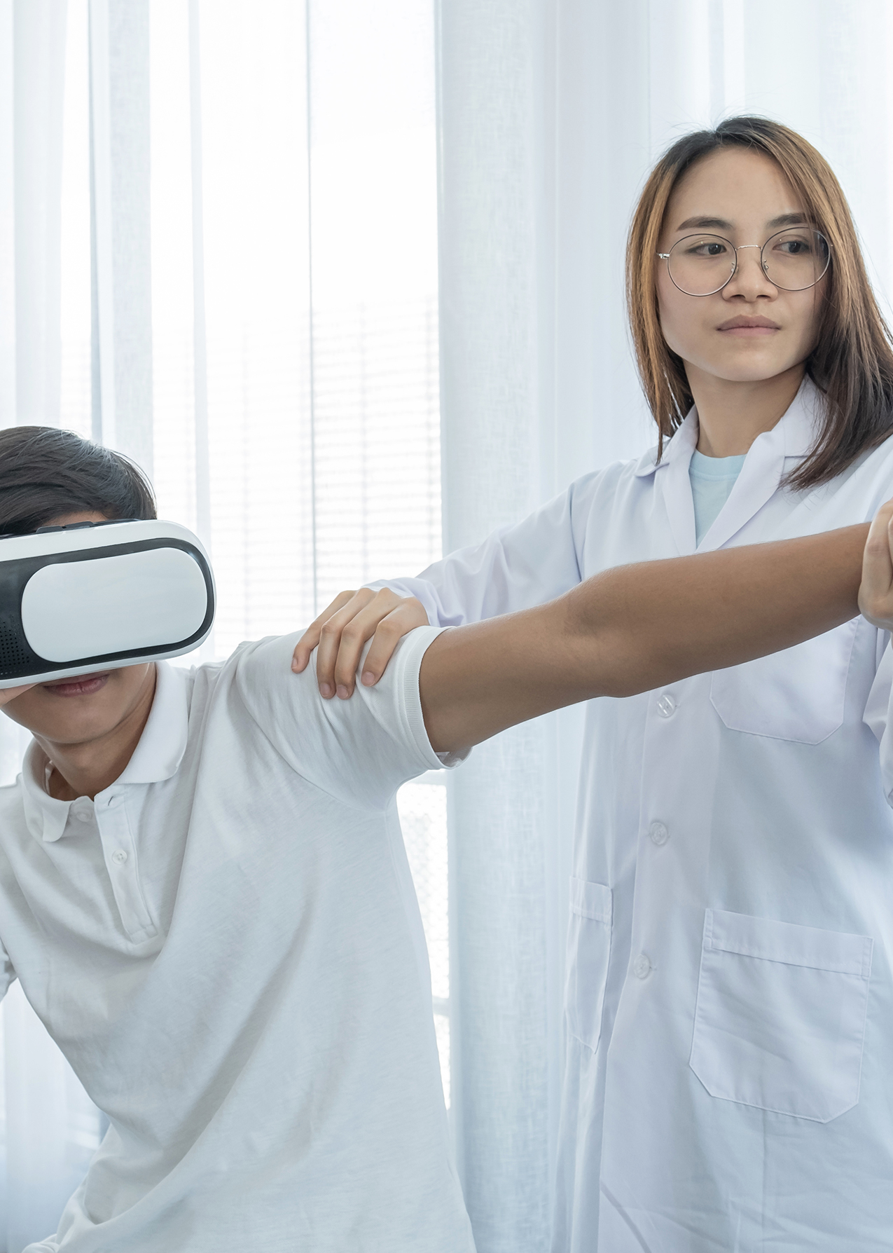 Young patient wearing a VR headset performing arm mobility exercises assisted by a healthcare professional using remotion.
