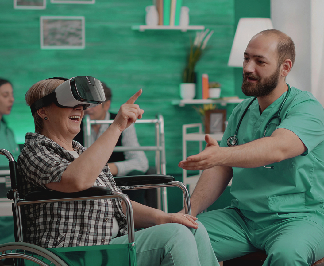 Male nurse guiding an elderly patient in a wheelchair during a Remotion virtual reality rehabilitation session in a nursing home.