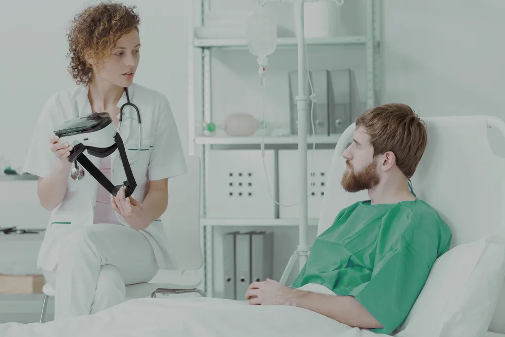 Healthcare professional showing a VR headset to a patient in a hospital bed for Remotion virtual rehabilitation therapy.